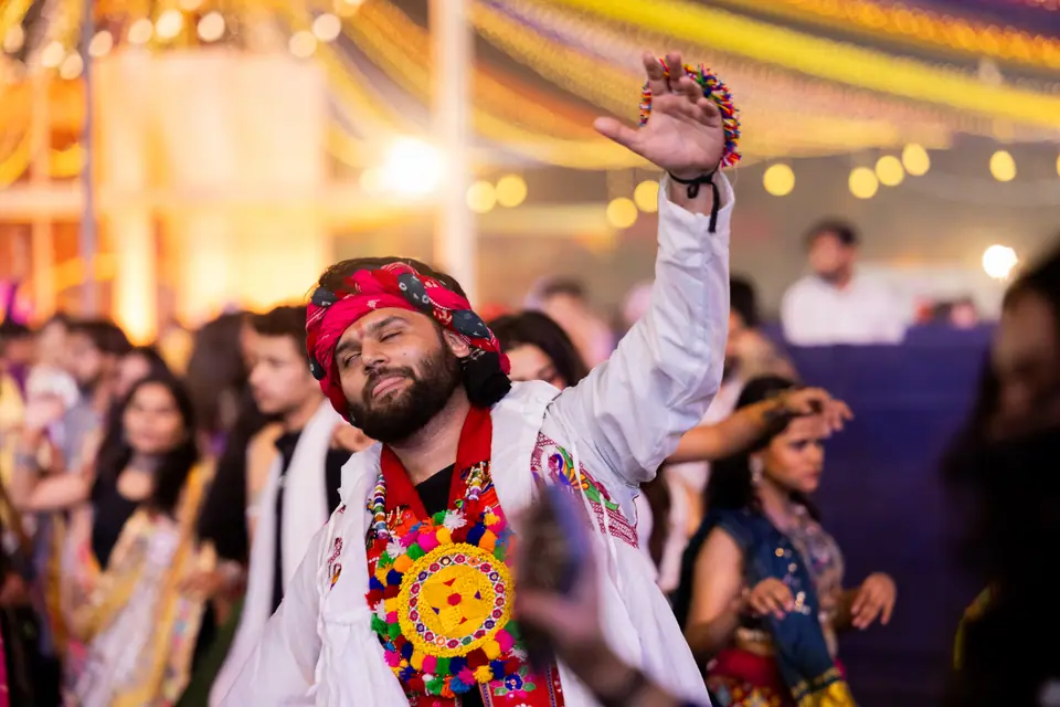 A khelaiya in a red turban and white kediyu dancing with one arm raised, eyes closed