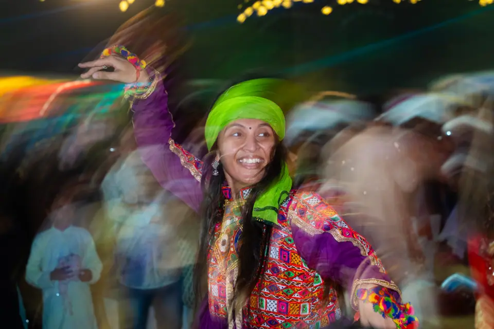 A dancer in a bright green turban laughing mid-garba, the crowd a blur behind her