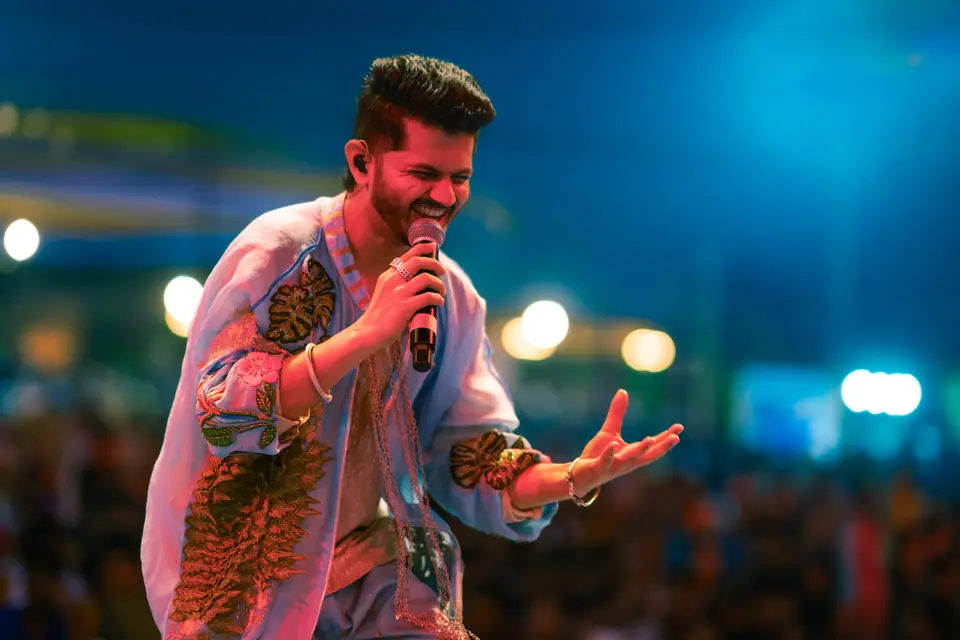 A singer in an embroidered kurta laughing into the microphone