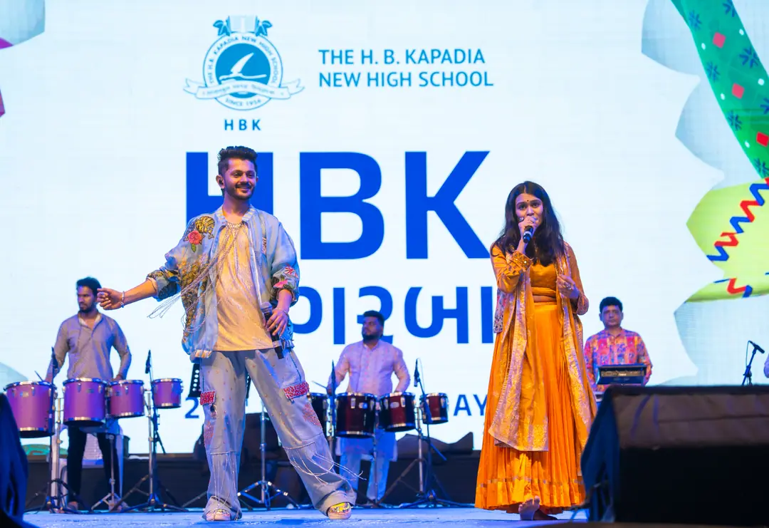 Two singers and the drummers on stage, HBK ના ગરબા and The H. B. Kapadia New High School on the LED wall behind them