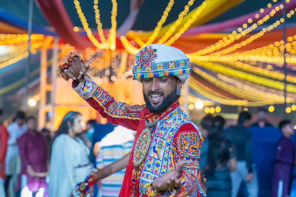 A khelaiya in an embroidered white turban and mirror-work kediyu dancing under the canopy lights