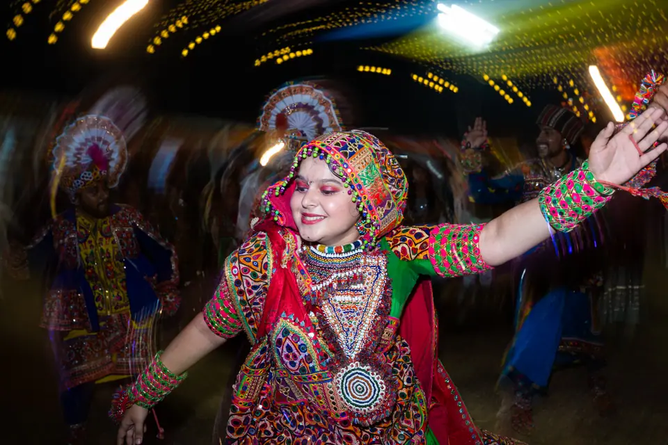 A dancer in a mirror-work chaniya choli, arms flung wide, smiling mid-spin
