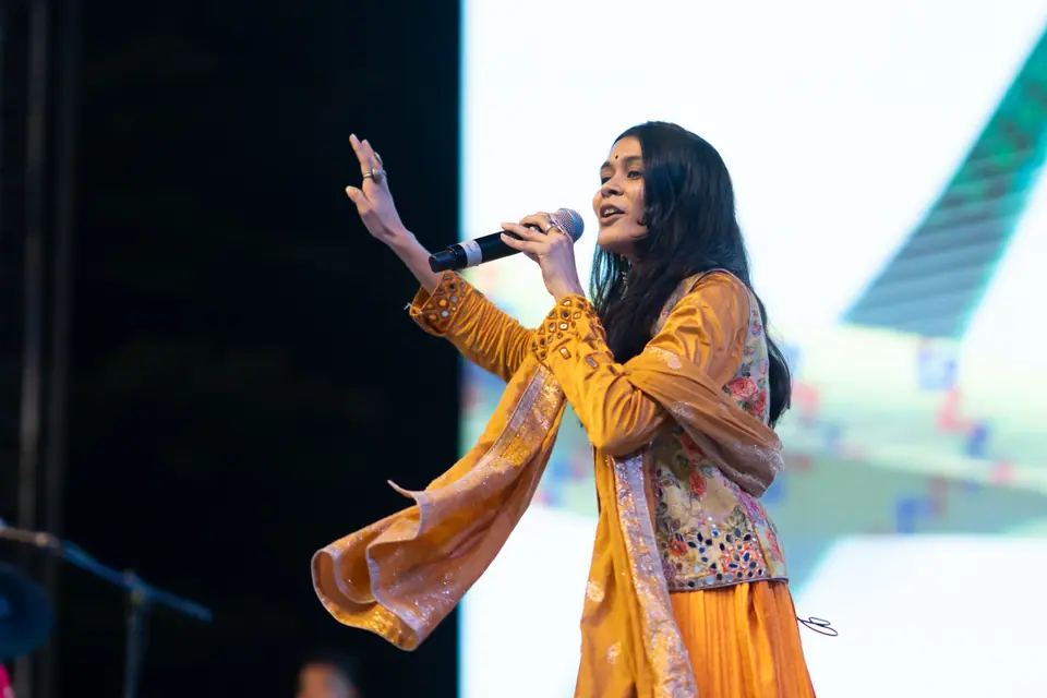 A singer in yellow singing on stage, one hand raised